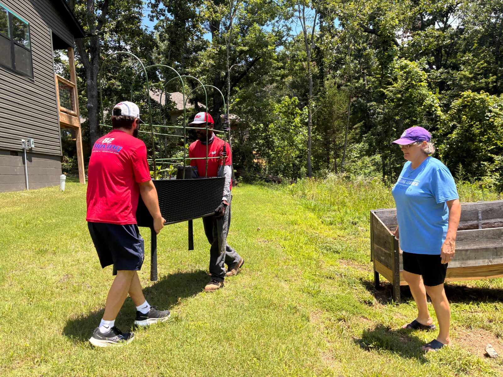 B2 movers Hunter and Dolph carrying outdoor furniture across a yard for a Bella Vista customer