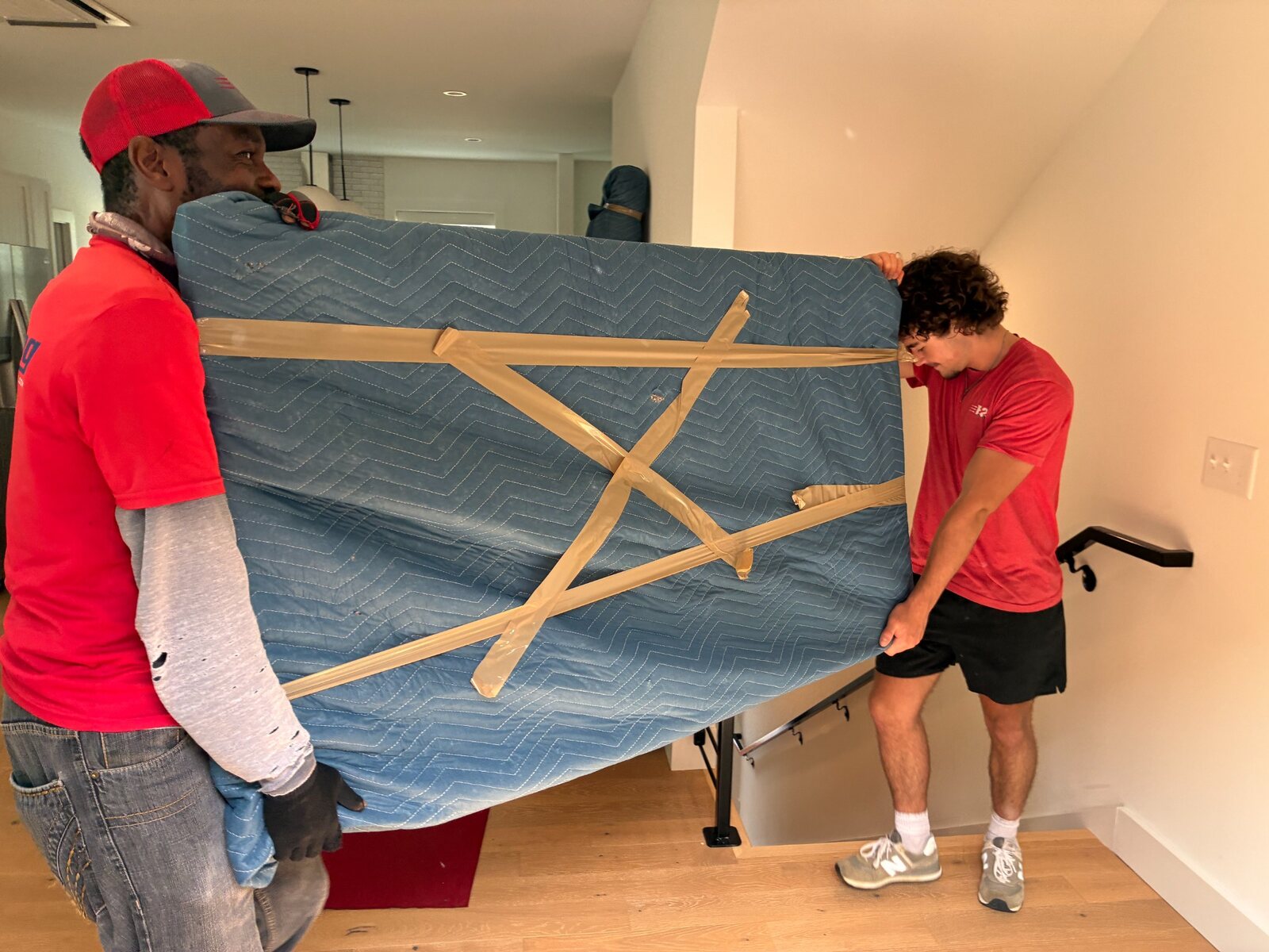 B2 movers Dolph and Jaxon carrying a padded household item down the stairs in a Bentonville townhome
