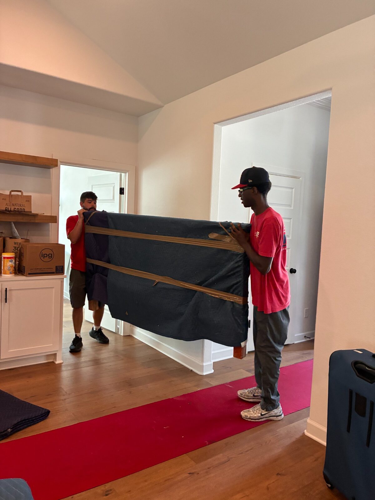 Two B2 movers carrying a padded and secured wooden footboard across protected flooring