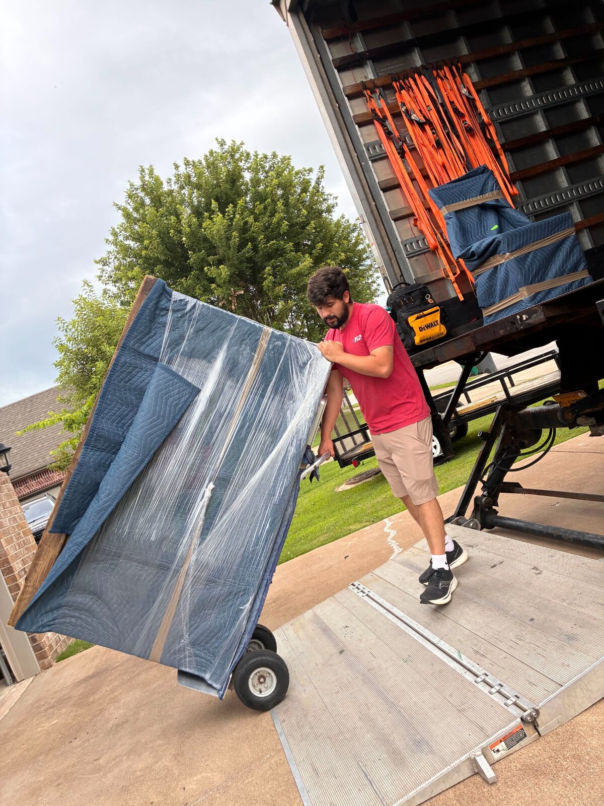 B2 mover Hunter guiding a padded wall cabinet onto a truck liftgate during a Rogers move